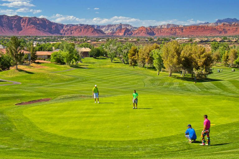 Cuatro hombres en ropa de colores brillantes en un verde en el campo de golf.