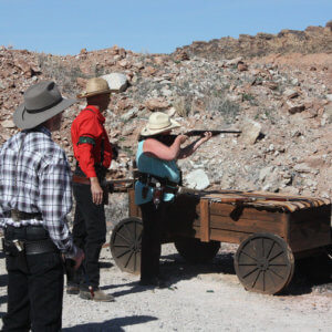 Crowd of men watching a woman fire a rifle