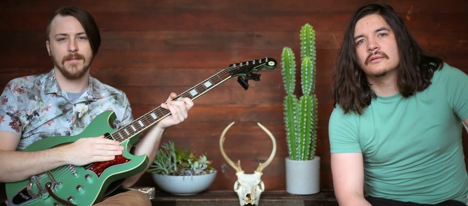 two men sitting by table, holding a guitar